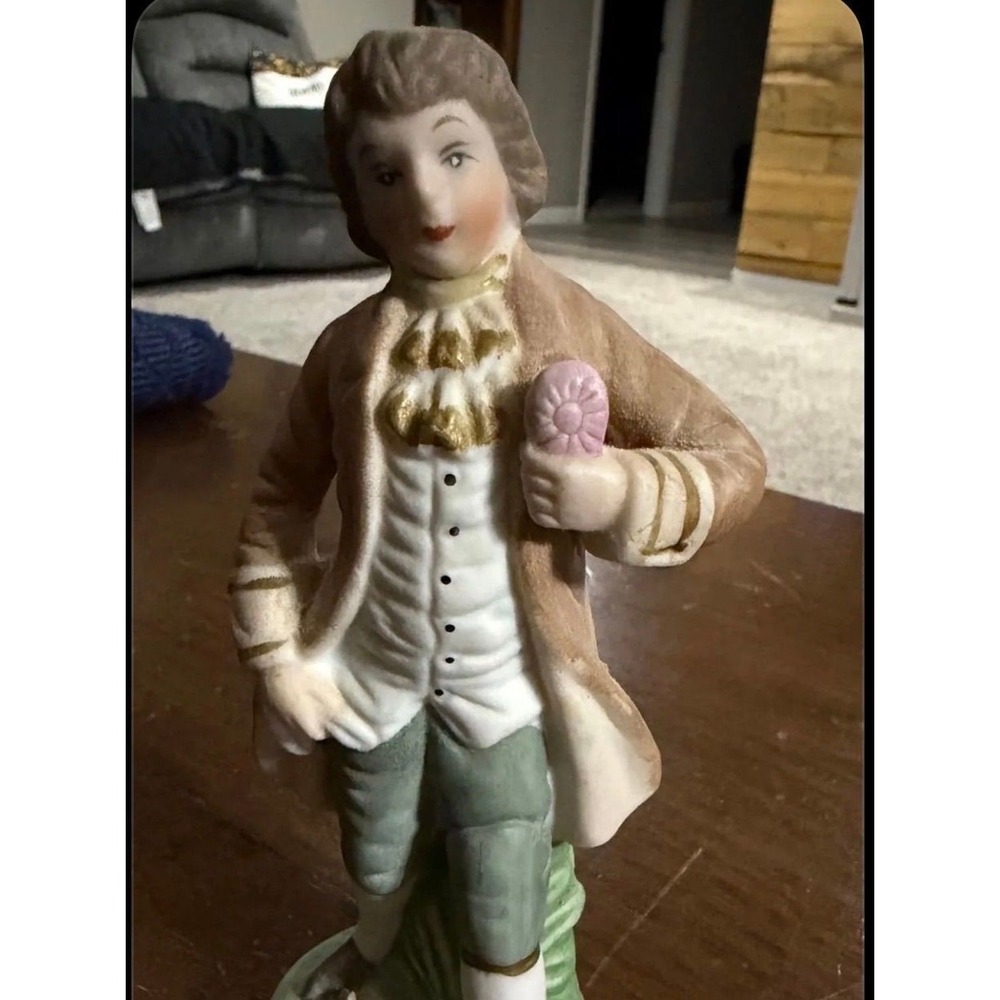 Vintage ceramic figurine is a colonial man holding a pink flower.